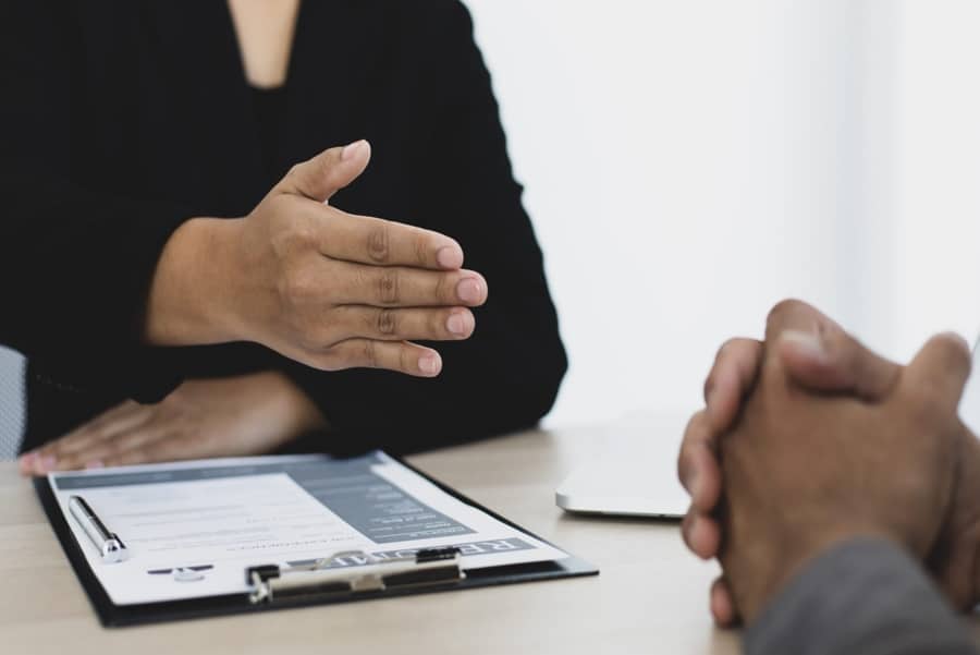 Professional Business Meeting Handshake Business professional extending a hand during a meeting with documents and a clipboard on the desk.