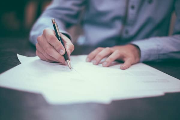 Signing Important Documents Close up of a person signing paperwork at a desk with a pen.